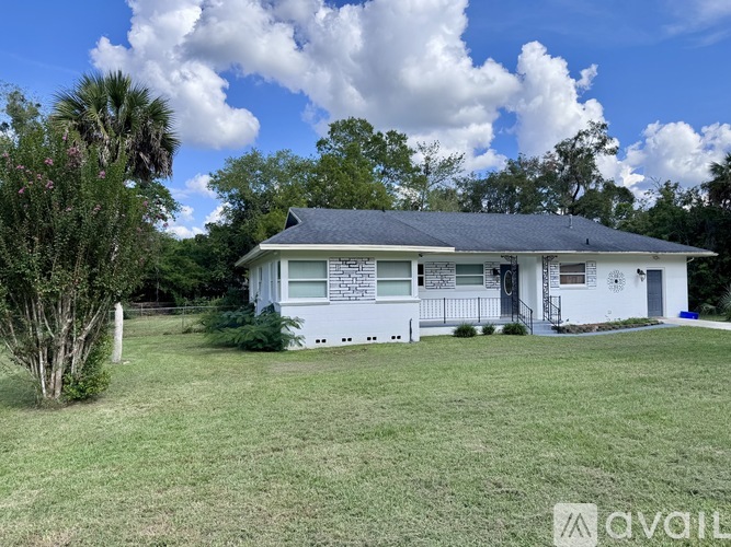 A house with a white exterior and a grey roof is surrounded by a grassy lawn and trees.
