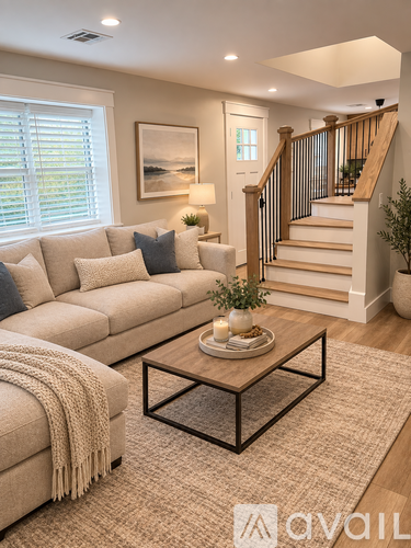 A living room with a beige couch, a coffee table, and a staircase.
