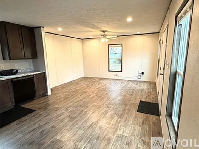 A living room with wooden flooring and a kitchen area to the left.