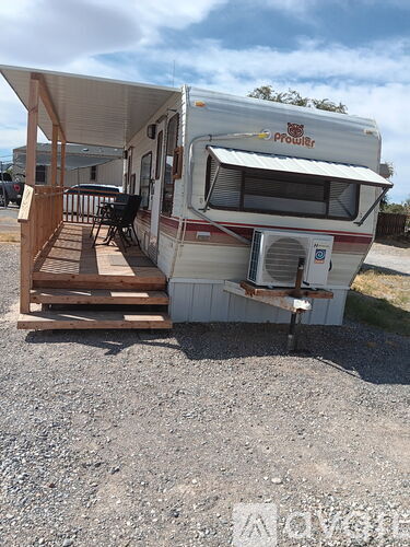 A white RV with a red logo on the side is parked on a gravel lot.