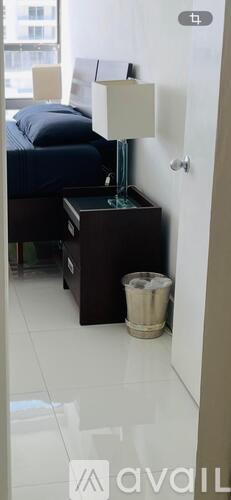 A bedroom with a bed, nightstand, and trash can.