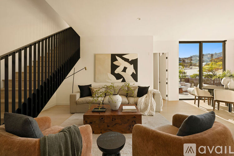 A living room with a large abstract painting on the wall and a view of the outdoors through the windows.