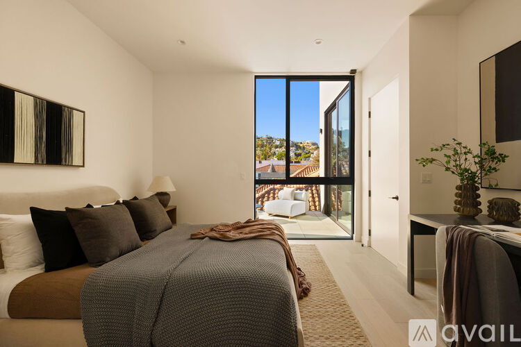 A bedroom with a large bed and a view of the outside through a glass door.