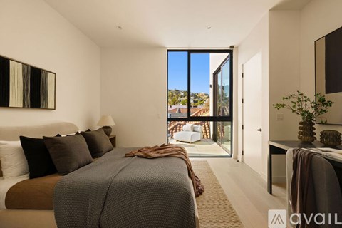 A bedroom with a large bed and a view of the outside through a glass door.