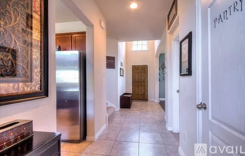 A hallway with a door on the right and a fridge on the left.