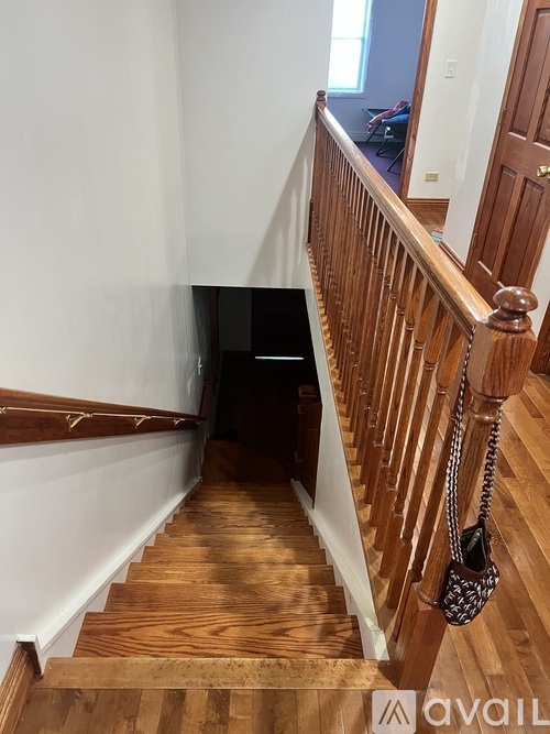 A staircase with a wooden handrail and a black bag hanging on it.