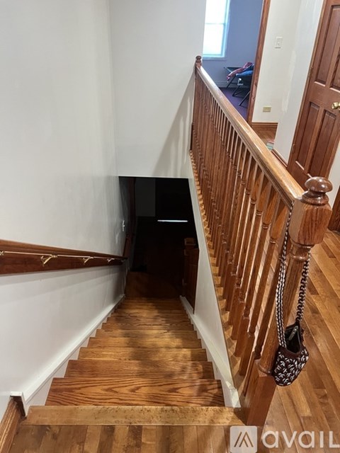 A staircase with a wooden handrail and a black bag hanging on it.