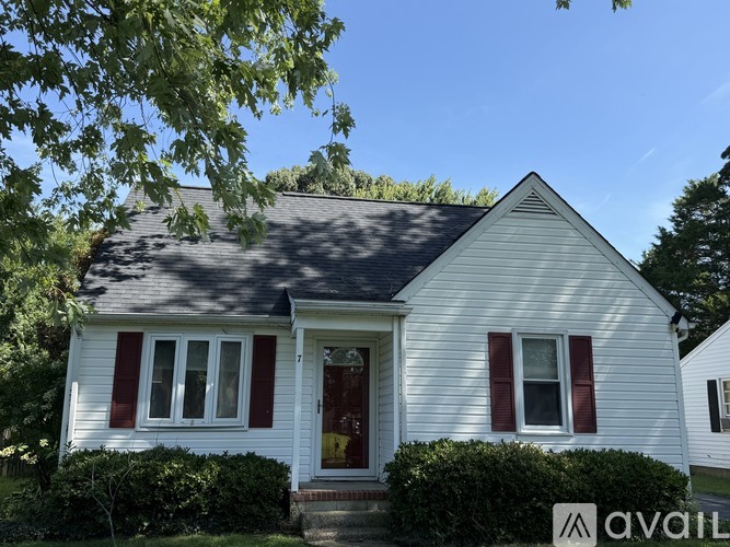 A white house with red shutters and a red door is for sale.