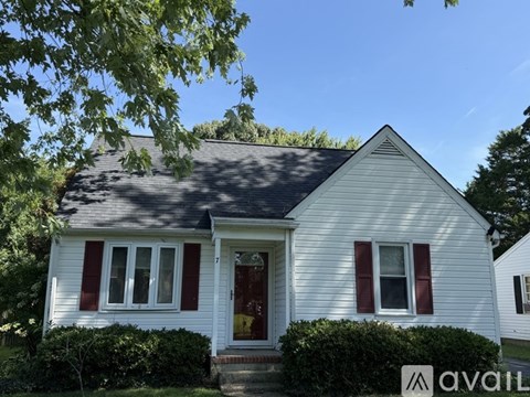 A white house with red shutters and a red door is for sale.