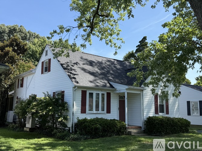 A white house with a red door and windows is surrounded by greenery.