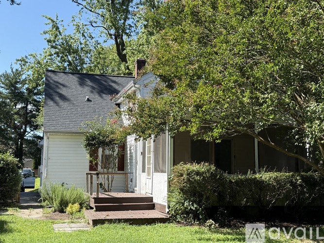 A house with a white exterior and a black roof is surrounded by greenery.