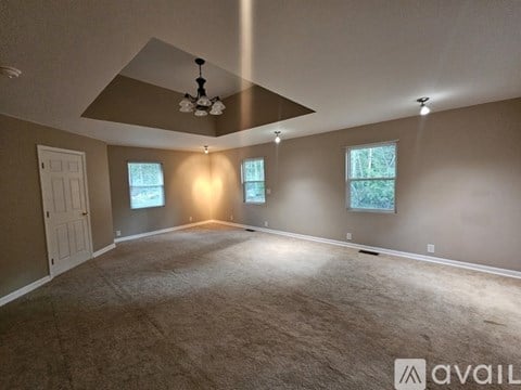 A spacious room with a carpeted floor, a ceiling fan, and three windows.
