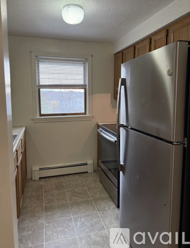A kitchen with a stainless steel refrigerator and a window with blinds.