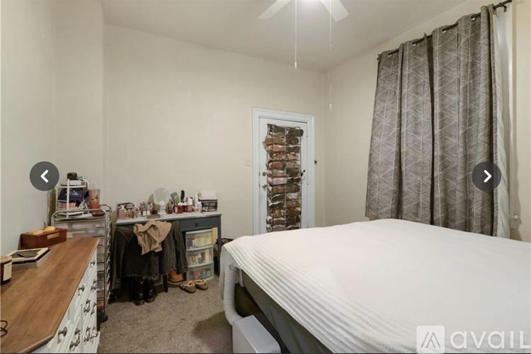 A bedroom with a bed, a desk, and a window with curtains.