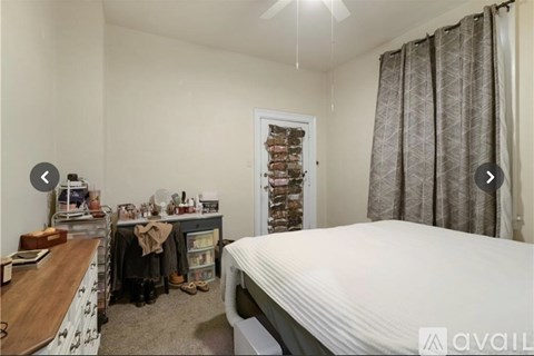 A bedroom with a bed, a desk, and a window with curtains.