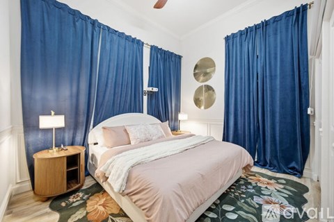 A bedroom with blue curtains and a white bed.
