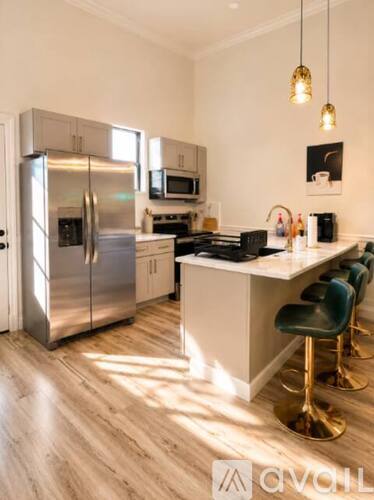 A modern kitchen with a stainless steel refrigerator, a microwave, a stove, and a bar area with four barstools.