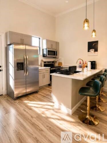 A modern kitchen with a stainless steel refrigerator, a microwave, a stove, and a bar area with four barstools.
