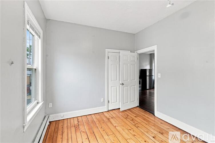A room with wooden floors and white walls, with a door open to another room.