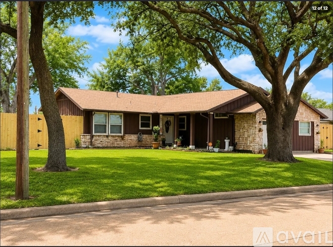 A house with a brown roof and a stone pillar is surrounded by a green lawn and trees.