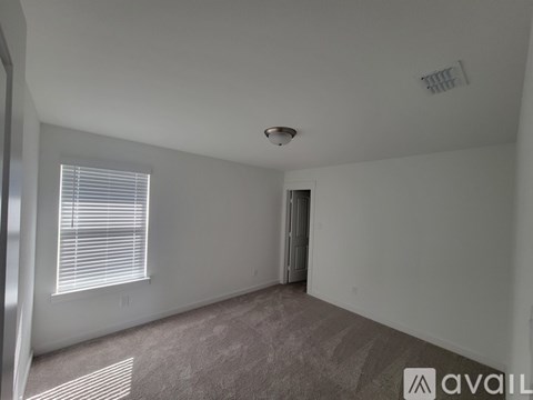 A room with a carpeted floor, a window with blinds, and a door leading to another room.