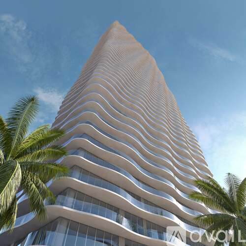 A tall, modern building with a curved design and palm trees in the foreground.