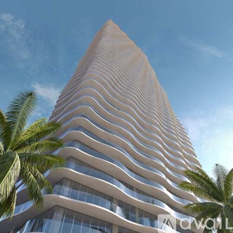 A tall, modern building with a curved design and palm trees in the foreground.