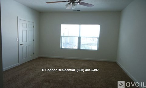 A room with a carpet floor, a ceiling fan, and a window with a view of a building.