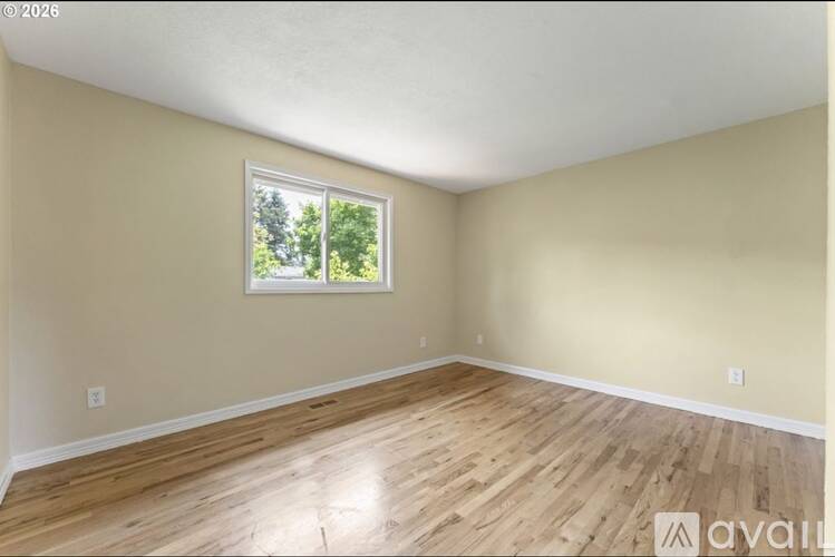 A room with wooden flooring and a window showing trees outside.
