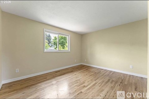 A room with wooden flooring and a window showing trees outside.