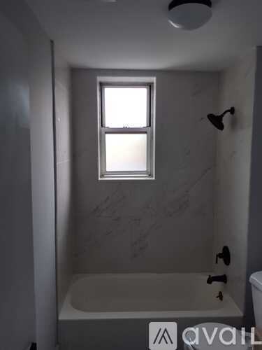 A bathroom with a tub, window, and a shower head.