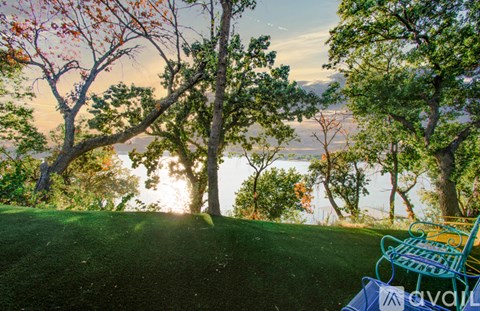 A bench is on a hill with trees and a body of water in the background.