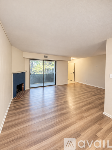A room with wooden flooring and a fireplace with a sliding glass door leading outside.