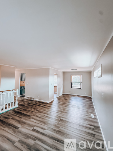 A spacious room with wooden flooring and white walls.
