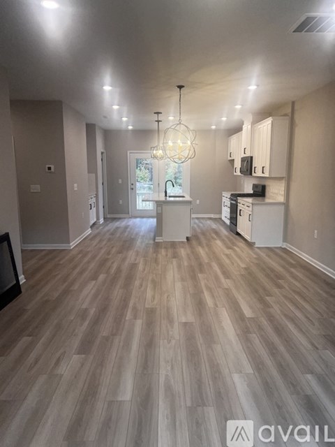 A spacious room with wooden flooring and a chandelier hanging from the ceiling.