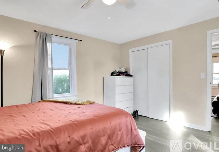 A bedroom with a pink bedspread and a window with curtains.