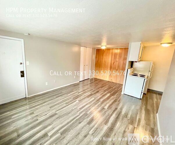 A room with wood flooring and a white refrigerator in the corner.