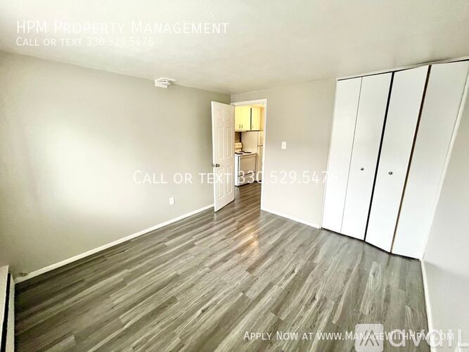 A room with wood flooring and a white wall with a doorway leading to another room.