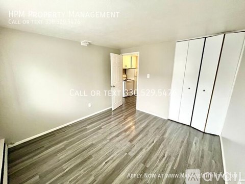 A room with wood flooring and a white wall with a doorway leading to another room.