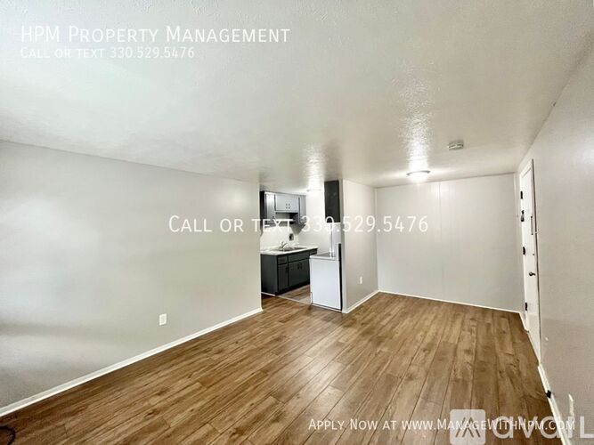 A room with wooden flooring and a white wall with a kitchenette in the background.