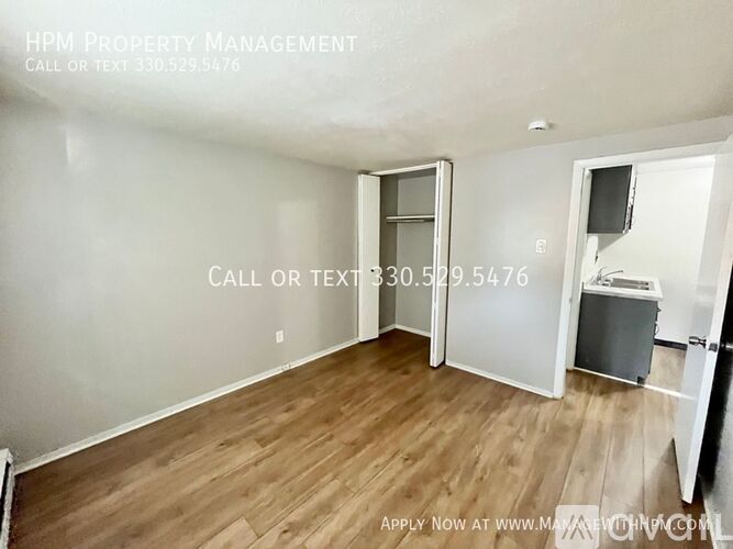 A room with wood flooring and a white wall with a doorway leading to another room.