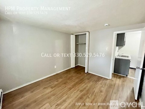 A room with wood flooring and a white wall with a doorway leading to another room.