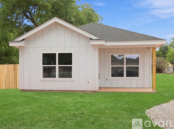 A small white house with a grey roof and a brown fence.