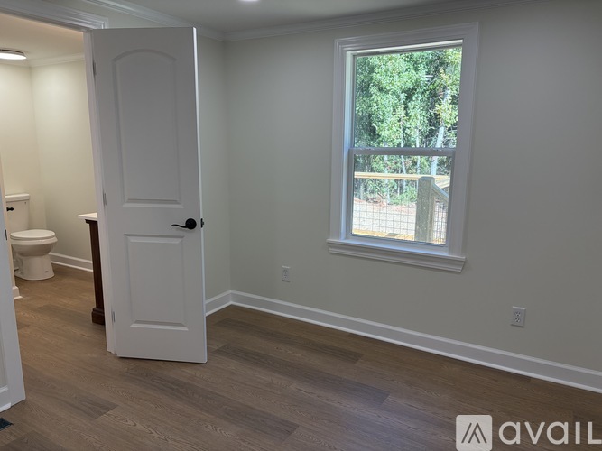 A room with a white door and a window with a view of trees.