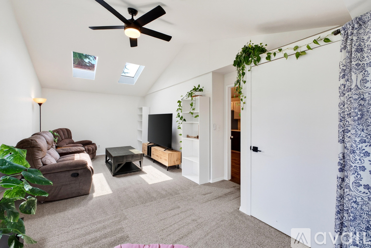 A living room with a brown couch, a coffee table, a flat screen TV, and a ceiling fan.