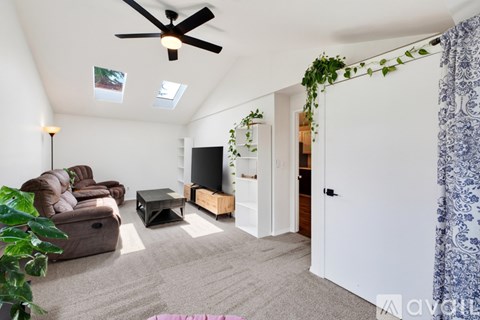 A living room with a brown couch, a coffee table, a flat screen TV, and a ceiling fan.