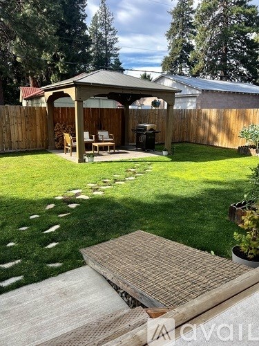 A wooden gazebo is surrounded by a wooden fence and a green lawn.