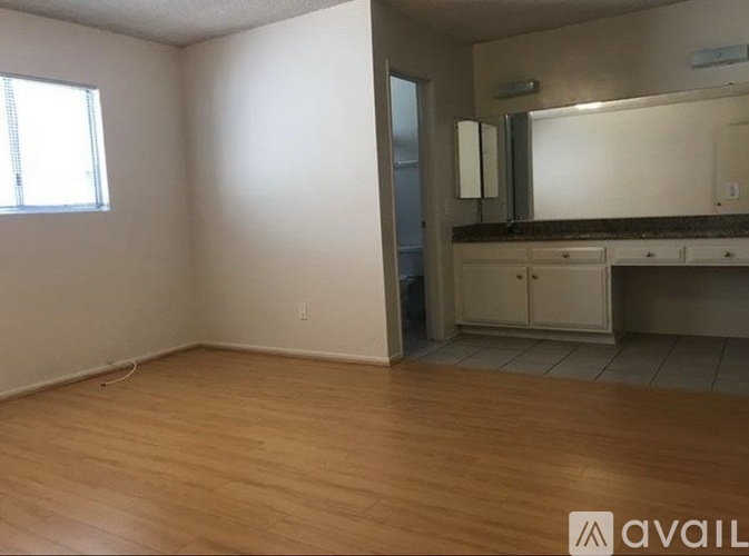 A room with wooden flooring and a bathroom area with a sink and mirror.