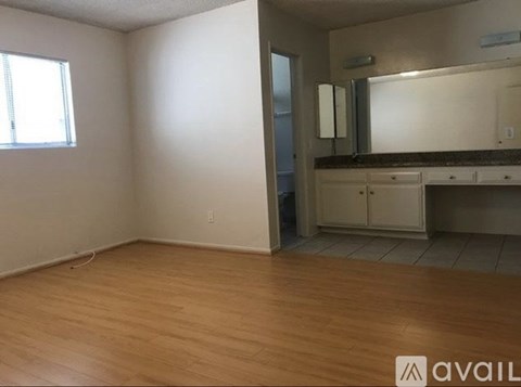 A room with wooden flooring and a bathroom area with a sink and mirror.