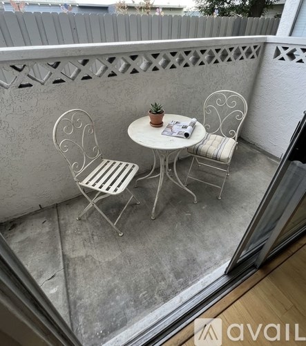 A small table with two chairs and a potted plant sits on a balcony.
